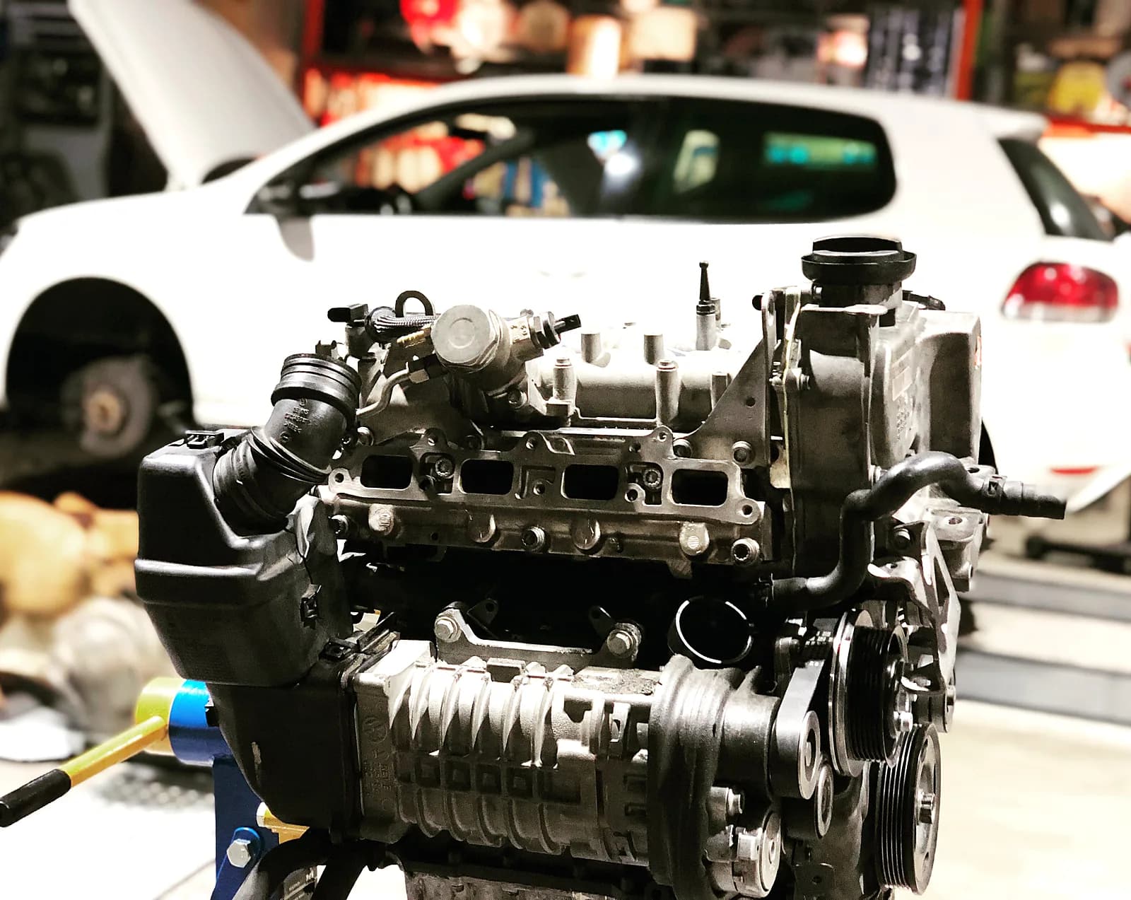 Ausgebauter VW 1.4 TSI Twincharger Motorblock vor weissem Golf in der Werkstatt