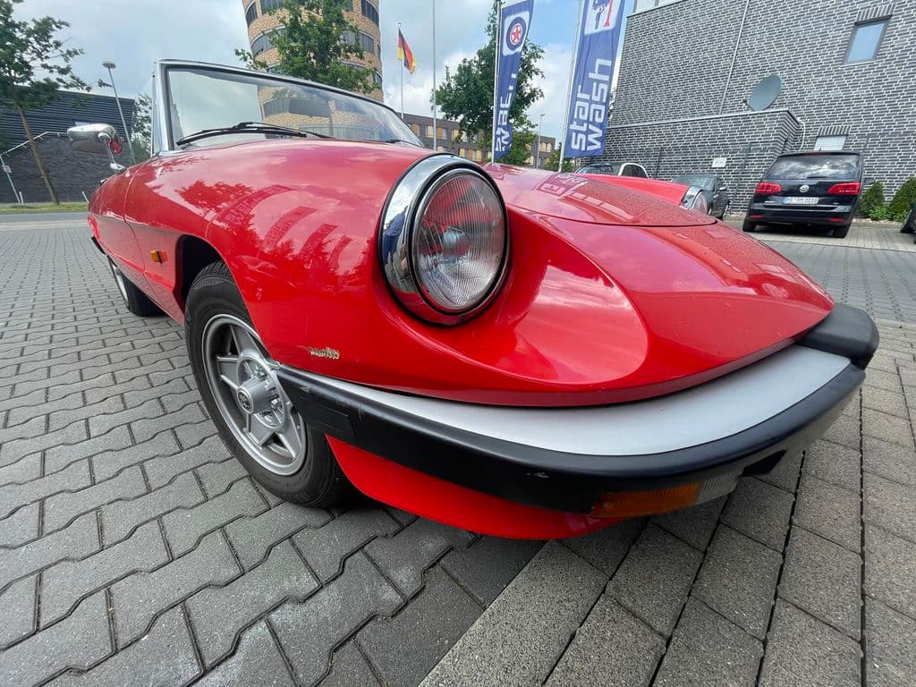 Roter Alfa Romeo Spider Oldtimer vor der Flagge.