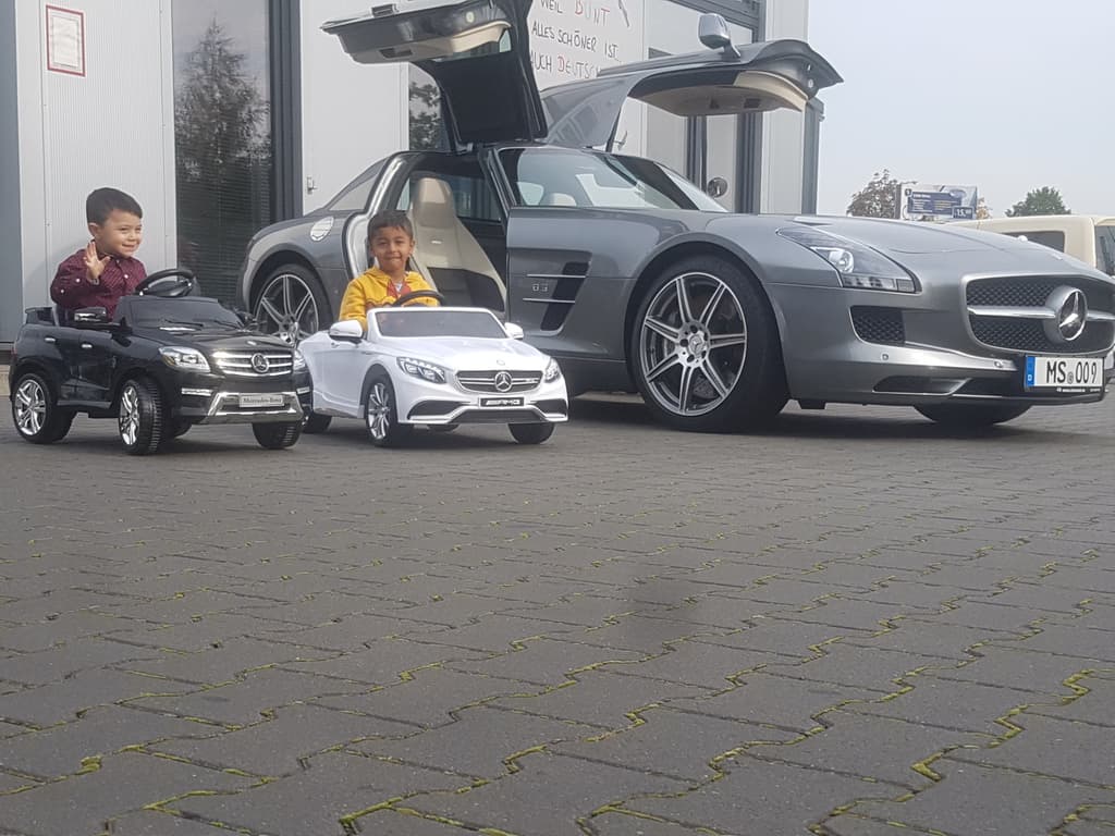 Kinder in Spielzeugautos vor einem echten Mercedes SLS.