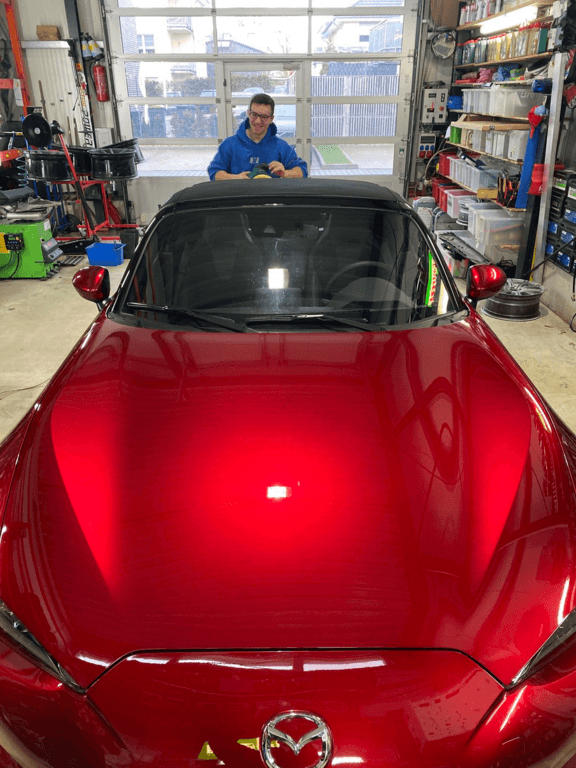 Roter Mazda MX-5 in der Werkstatt, Techniker im Hintergrund.