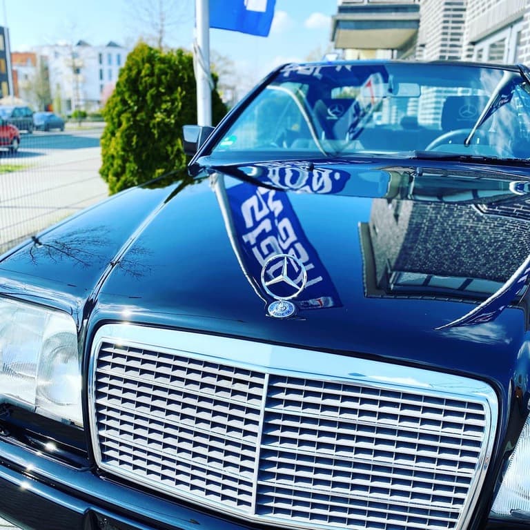 Dunkles Mercedes-Coupé mit Stern und Werbefahne im Hof.