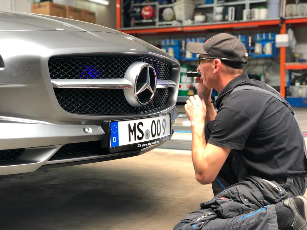 Techniker prüft Mercedes-Front mit Taschenlampe.