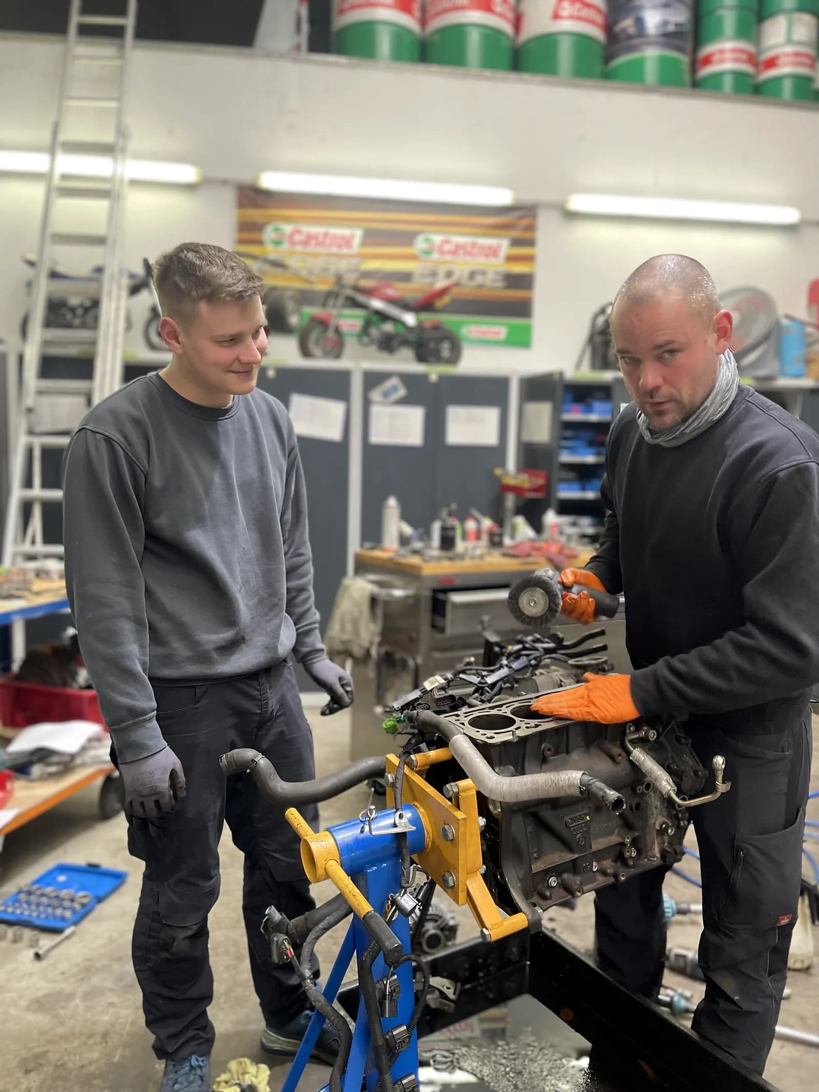 Zwei Mitarbeiter arbeiten an einem ausgebauten Motor mit orangen Handschuhen